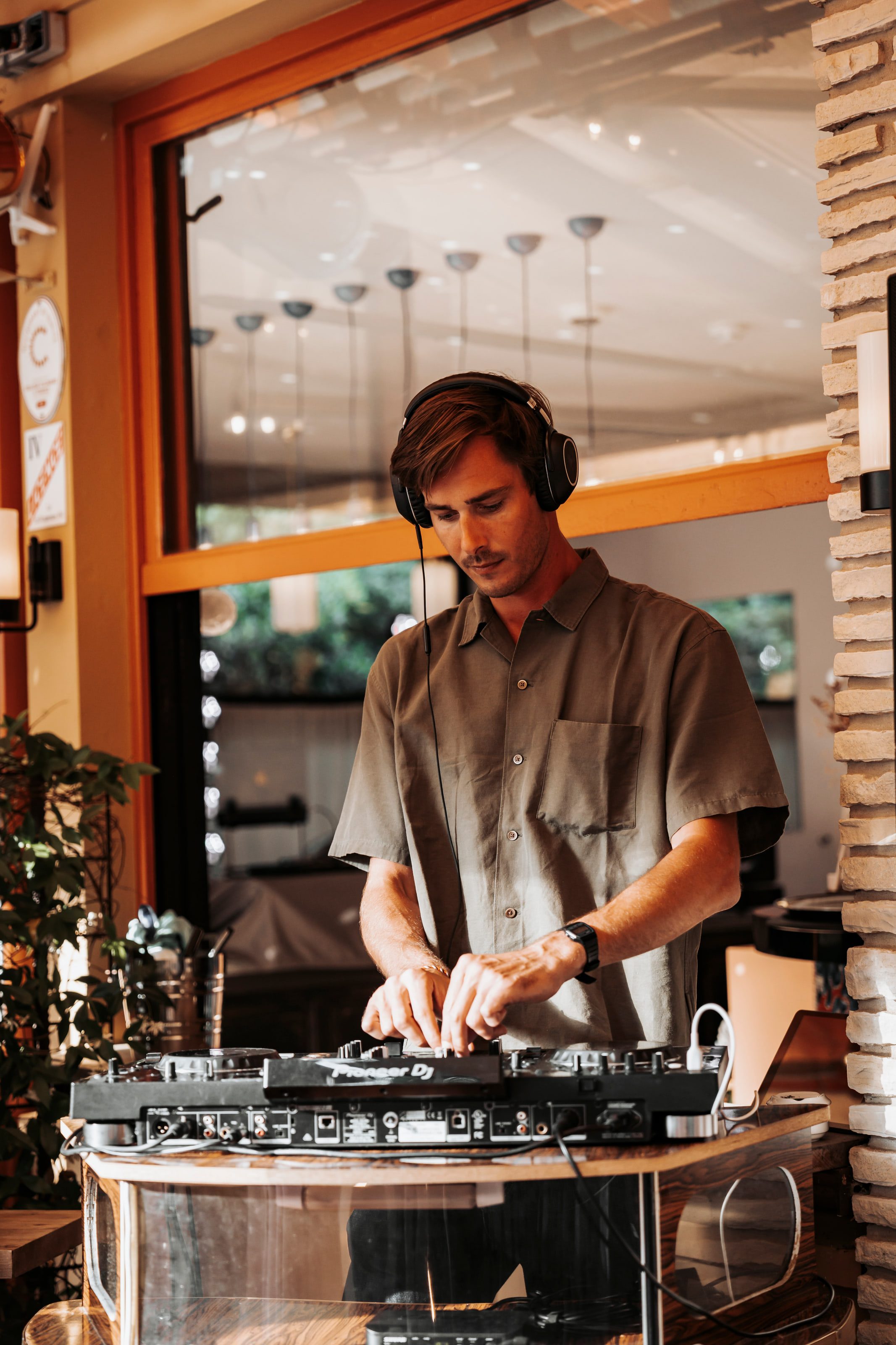 Black and white portrait of Denver mixing at the decks, headphones on, beneath a canopy of pendant lights.